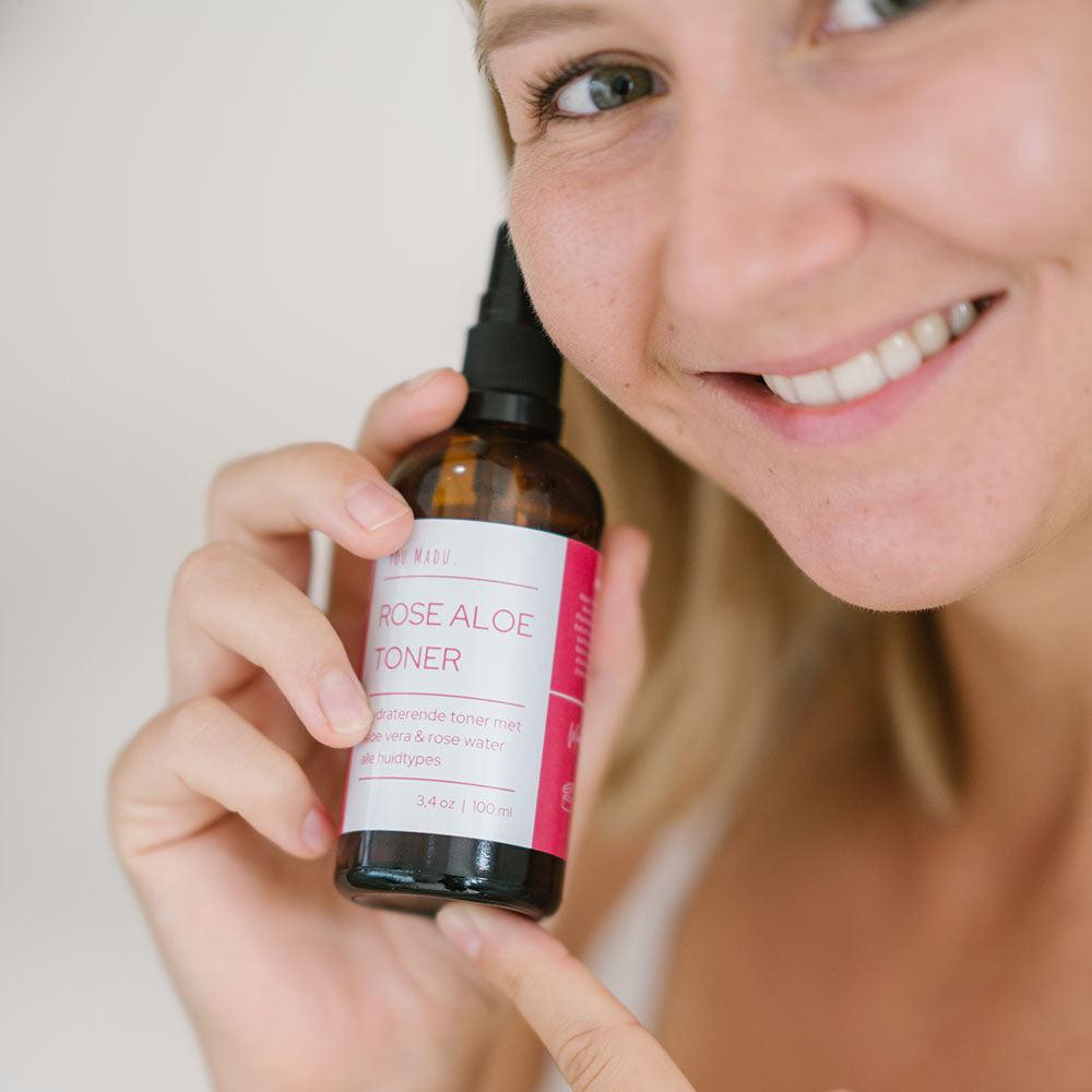 Een vrouw houdt een fles Rose Aloe Toner vast, een natuurlijke toner met aloë vera en rozenextract om de huid te reinigen en te hydrateren.